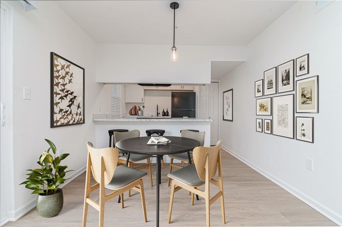 Bright and modern dining area with elegant round table, comfortable chairs, and open-concept kitchen with stylish art decor and abundant natural light.