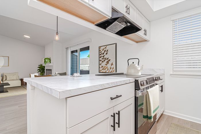 Modern kitchen with sleek marble countertops, white cabinetry, and a cozy open-plan living room with abundant natural light.