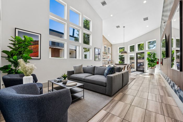 Bright and modern living area with large windows, sleek gray sofas, and a stylish dining space offering abundant natural light and contemporary decor.