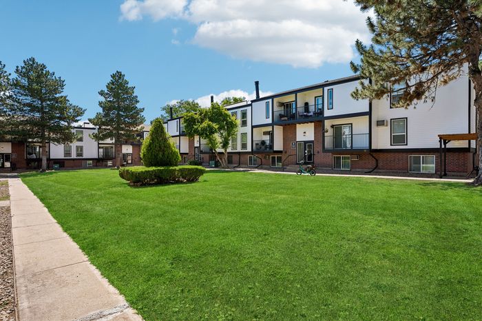 Inviting apartment complex with modern balconies surrounded by lush green lawns and mature trees.