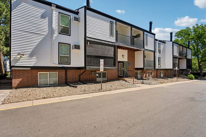 Modern apartment complex with sleek white and brick exterior, featuring private balconies and contemporary design nestled in a peaceful neighborhood.