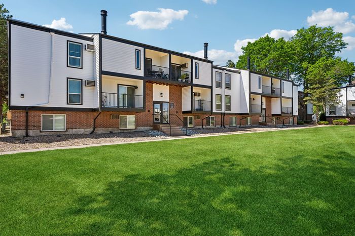 Charming multi-story apartment building with modern design, oversized windows, and lush green landscaping.