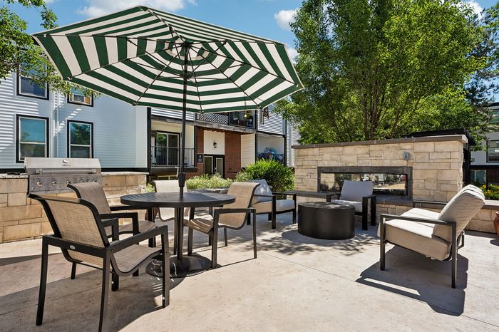 Charming outdoor patio with modern furniture, a cozy fire pit, and a chic striped umbrella, perfect for al fresco dining and relaxation.