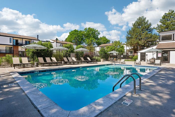 Inviting outdoor pool area with cozy lounge chairs, large umbrellas, and lush greenery under a bright blue sky.