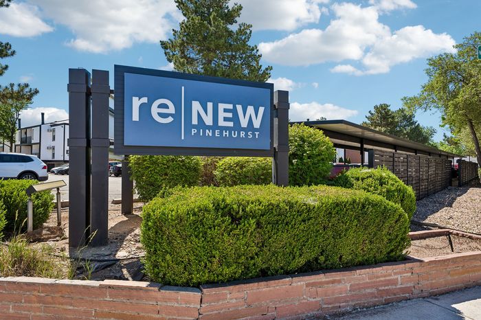 Inviting entrance to reNEW Pinehurst with lush greenery and modern signage under a clear blue sky.