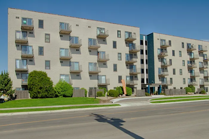 Modern apartment building with multiple balconies, lush greenery, and clear blue skies.