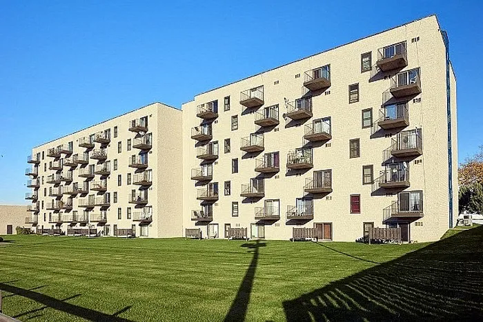 Modern apartment complex with multiple balconies and lush green space under a clear blue sky, offering a serene living environment.