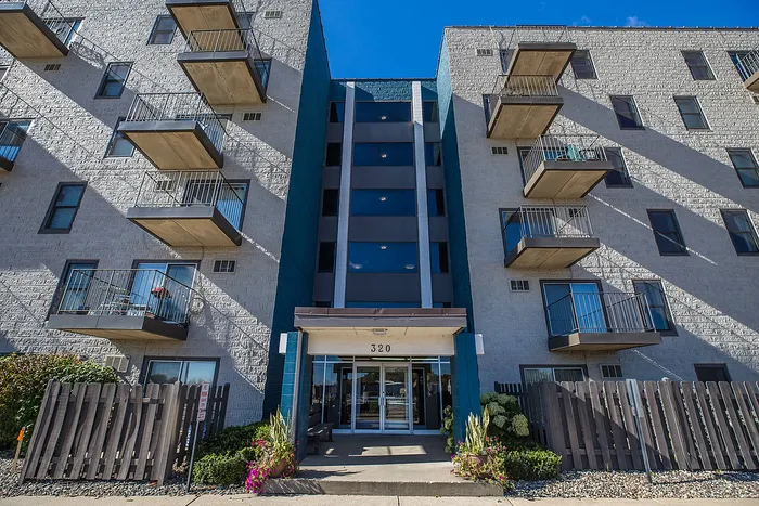 Contemporary apartment complex with private balconies, sleek entrance, and vibrant landscaping under a clear blue sky.