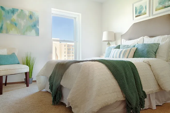 Bright and inviting bedroom featuring plush bedding, chic d&eacute;cor, and a large window with a stunning urban view.