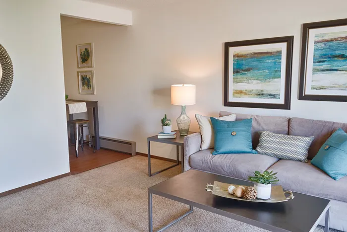 Inviting living room with modern gray sofa adorned with blue and patterned cushions, complemented by stylish artwork and a sleek coffee table.