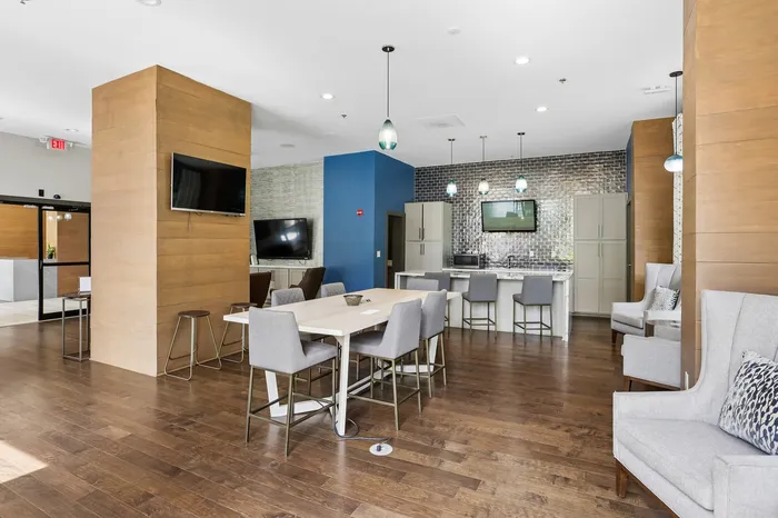 Modern communal area featuring sleek hardwood floors, stylish dining tables, plush seating, and a contemporary kitchen with pendant lighting.
