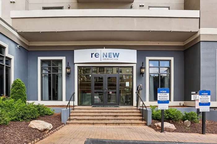 Inviting entrance of ReNew Perimeter View with modern architecture, lush greenery, and designated parking signs for future residents.