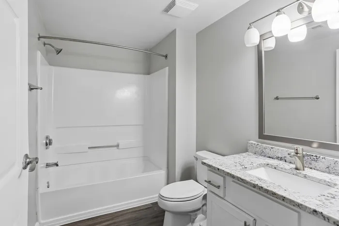 Modern bathroom featuring sleek white fixtures, a granite countertop, and elegant lighting, offering a clean and inviting atmosphere.