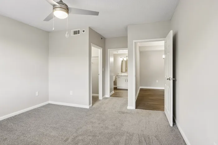 Modern apartment interior featuring a bright room with plush carpeting, ceiling fan, and access to a sleek bathroom with elegant lighting.