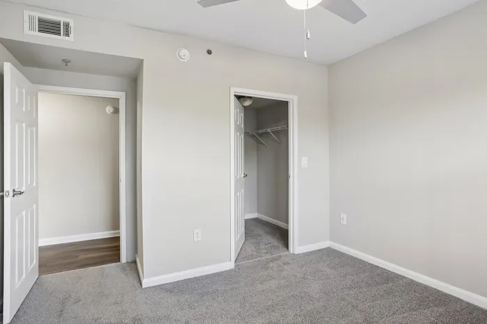 Bright and spacious bedroom with plush carpeting, a modern ceiling fan, and a convenient walk-in closet, perfect for cozy living.