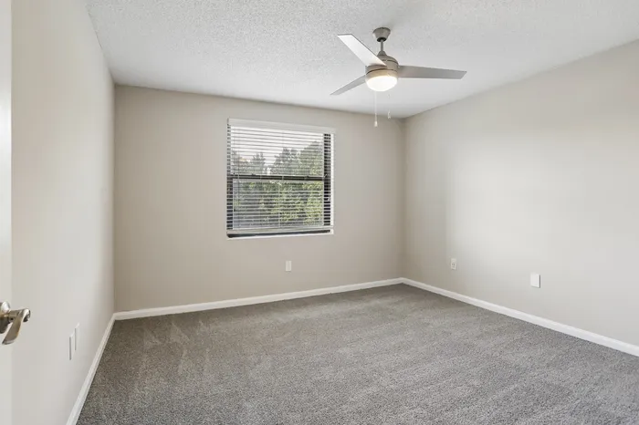 Charming bedroom with plush carpet, large window, and ceiling fan offering a serene view of greenery.