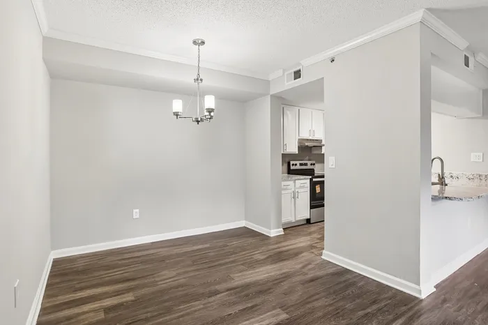 Modern living space featuring elegant hardwood floors, a chic chandelier, and a sleek white kitchen with stainless steel appliances.