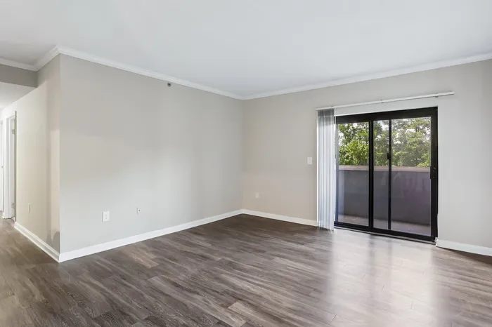 Bright and spacious living area with elegant wood flooring and large glass doors leading to a serene balcony view.