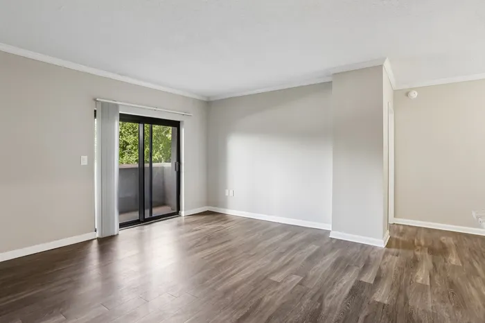 Inviting open-plan living area with elegant wood flooring and glass doors leading to a serene balcony view.