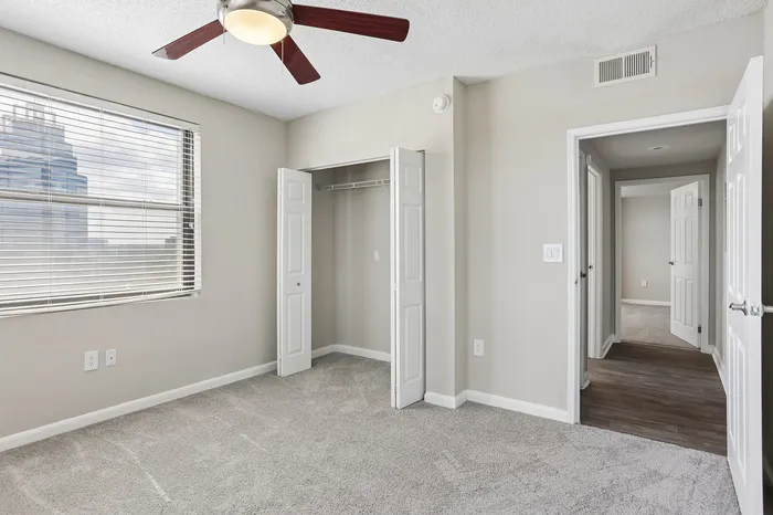 Bright bedroom with plush carpeting, a ceiling fan, and spacious closet in a modern apartment.