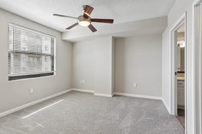 Bright, cozy bedroom with soft carpeting, modern ceiling fan, and abundant natural light from large window.