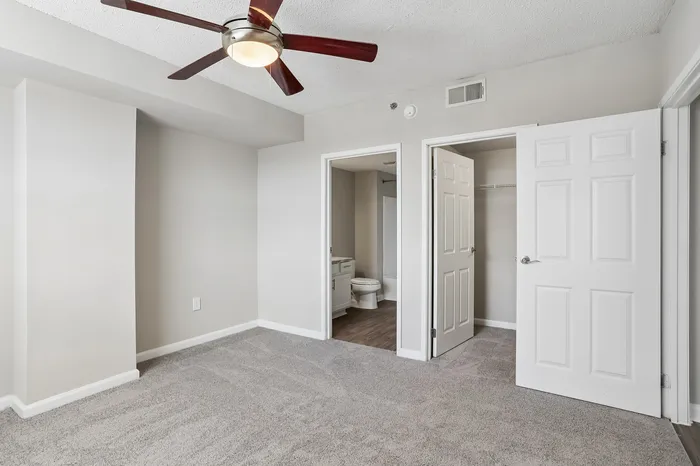 Modern bedroom with plush carpet, ceiling fan, and en-suite bathroom, perfect for comfort and relaxation.