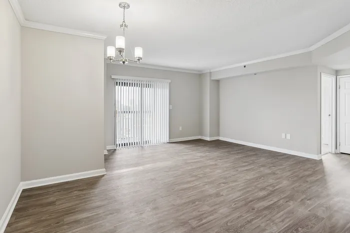 Bright and spacious living area with elegant light fixture, sleek wooden flooring, and large sliding glass doors leading to a balcony.