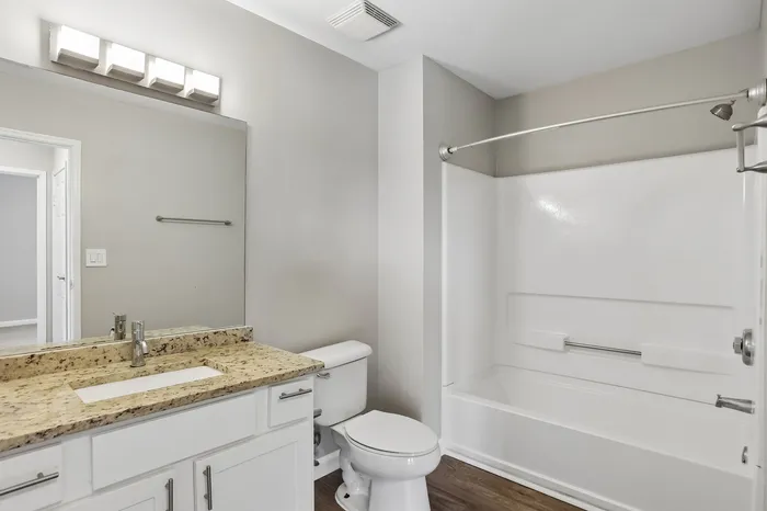 Modern bathroom featuring sleek granite countertops, elegant vanity lighting, and a pristine bathtub with shower.