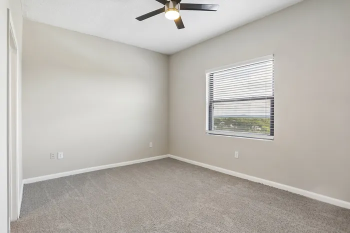 Bright, spacious bedroom with plush carpet and large window with scenic view, featuring modern ceiling fan.