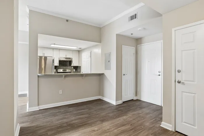 Modern apartment entryway with sleek hardwood floors and a view into the bright, fully-equipped kitchen.