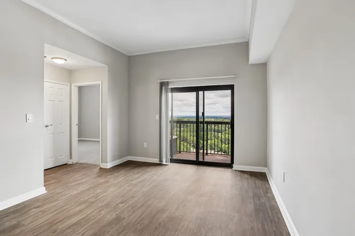 Bright living room with sleek laminate flooring, large sliding glass doors leading to a balcony with a scenic view, ideal for modern living.