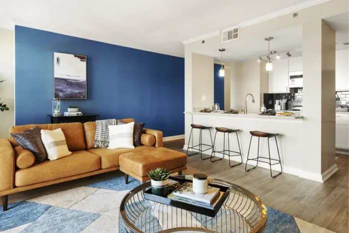 Chic living space with a contemporary tan sofa, stylish blue accent wall, and a modern kitchen island with seating.