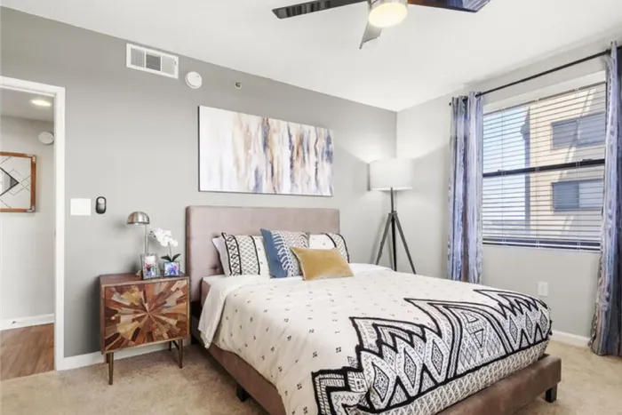 Bright and inviting bedroom with stylish bedding, modern artwork, and abundant natural light from large window.