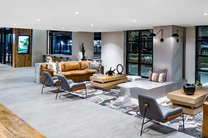 Modern and inviting lounge area featuring a stylish brown leather sofa, sleek grey chairs, and contemporary decor in a bright setting.