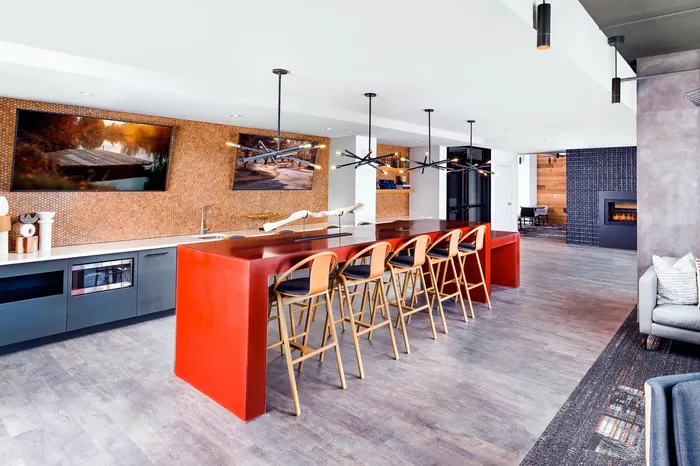 Modern apartment kitchen and living area with vibrant red island, elegant wooden bar stools, chic pendant lighting, and cozy fireplace.