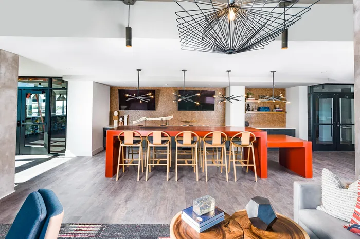 Modern communal area with a sleek bar counter and stylish barstools, featuring contemporary lighting and vibrant decor in a spacious and inviting setting.