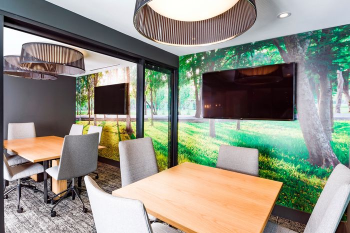 Modern meeting area with natural ambiance, featuring wooden tables, stylish gray chairs, and scenic forest wall mural for an inspiring workspace.