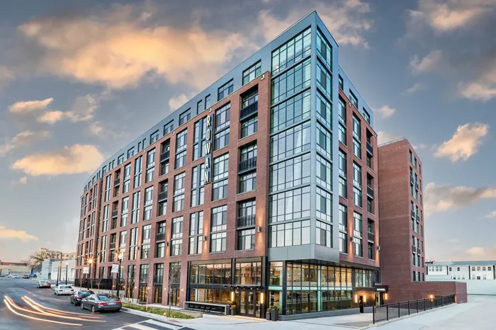 Modern urban apartment building with sleek glass facade and elegant brick architecture against a picturesque sky.