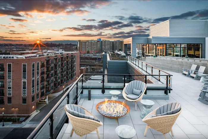 Luxurious rooftop terrace with cozy seating, fire pit, and panoramic city views at sunset.