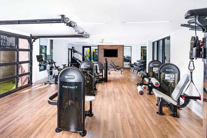 Luxe apartment gym featuring state-of-the-art exercise equipment, sleek wooden flooring, and abundant natural light.