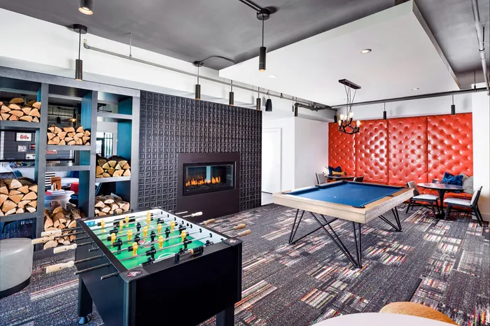 Contemporary entertainment room with chic fireplace, vibrant red wall seating, a pool table, and foosball table, perfect for relaxation and fun.