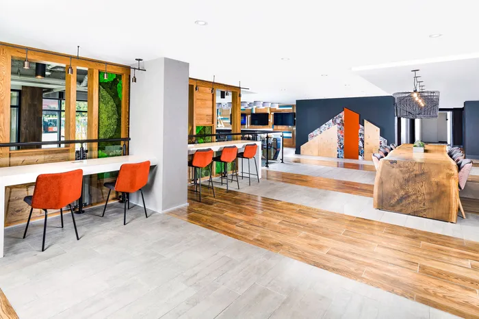 Chic and modern communal space showcasing vibrant orange seating, sleek workstations, and an inviting wooden dining table.