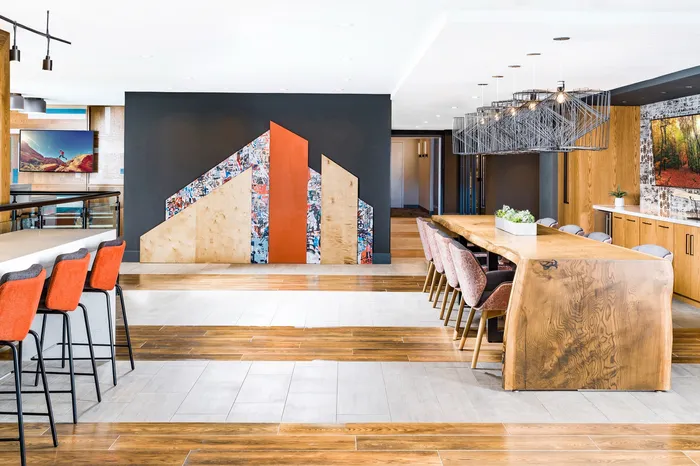 Modern communal living space showcasing a long rustic wooden dining table, vibrant orange seating, and contemporary artistic wall decor.