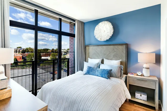 Inviting bedroom with a plush bed, vibrant blue accent wall, and large windows offering a stunning urban view.