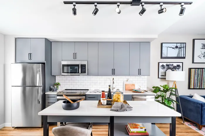 Modern kitchen with sleek gray cabinets, stainless steel appliances, and stylish track lighting, accented by contemporary art and a cozy lounge area.