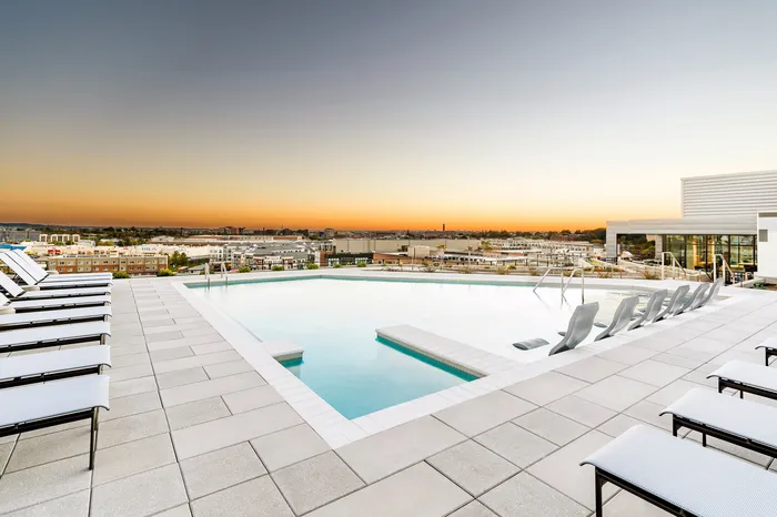 Luxurious rooftop pool area with panoramic city views at sunset, featuring elegant sun loungers and a serene atmosphere.