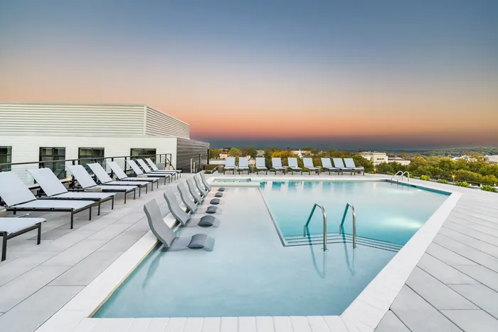 Luxurious rooftop pool with stylish lounge chairs overlooking a breathtaking sunset view.