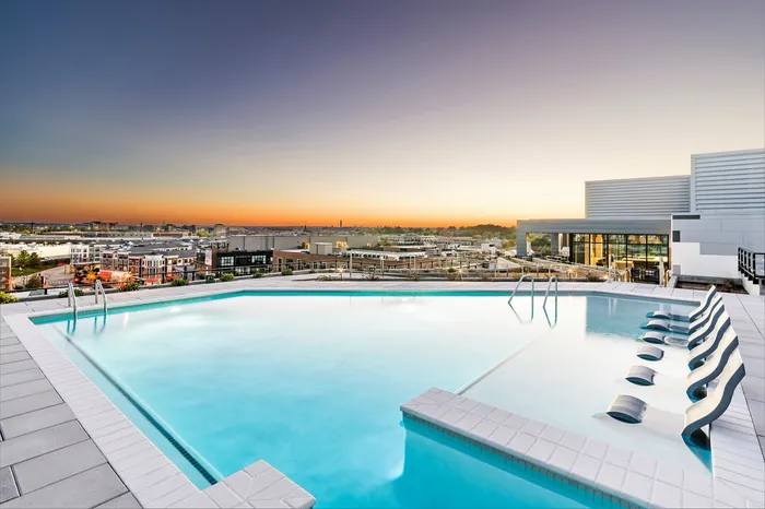 Luxurious rooftop pool with sleek lounge chairs offering breathtaking sunset views over a vibrant cityscape.