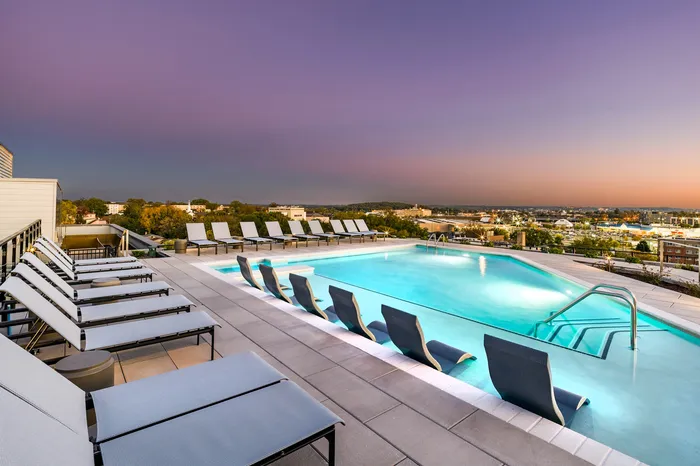 Luxurious rooftop pool with modern lounge chairs overlooking a stunning cityscape at sunset.