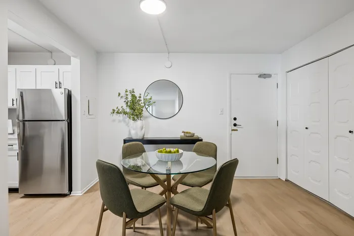 Chic dining area with a round glass table, modern green chairs, and elegant decor in a contemporary apartment.